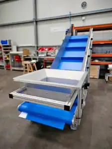 Convoyeur à bande incliné avec tasseaux, rives latérales et piètement sur roulettes en atelier industriel, fabrication Arcane France